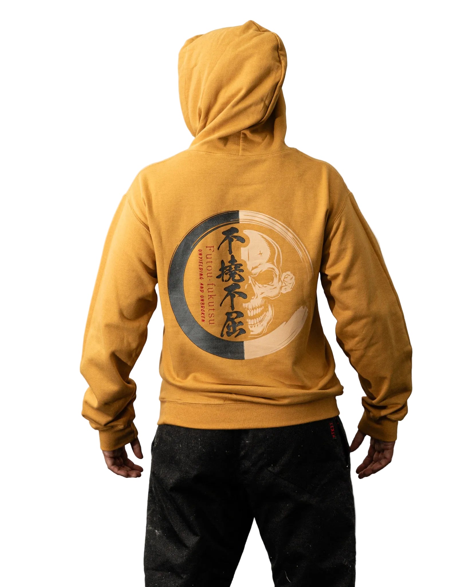 A person shown from the back wearing a mustard yellow hoodie with a large circular graphic print on the back in black, gray, and beige, paired with black pants against a plain white background.